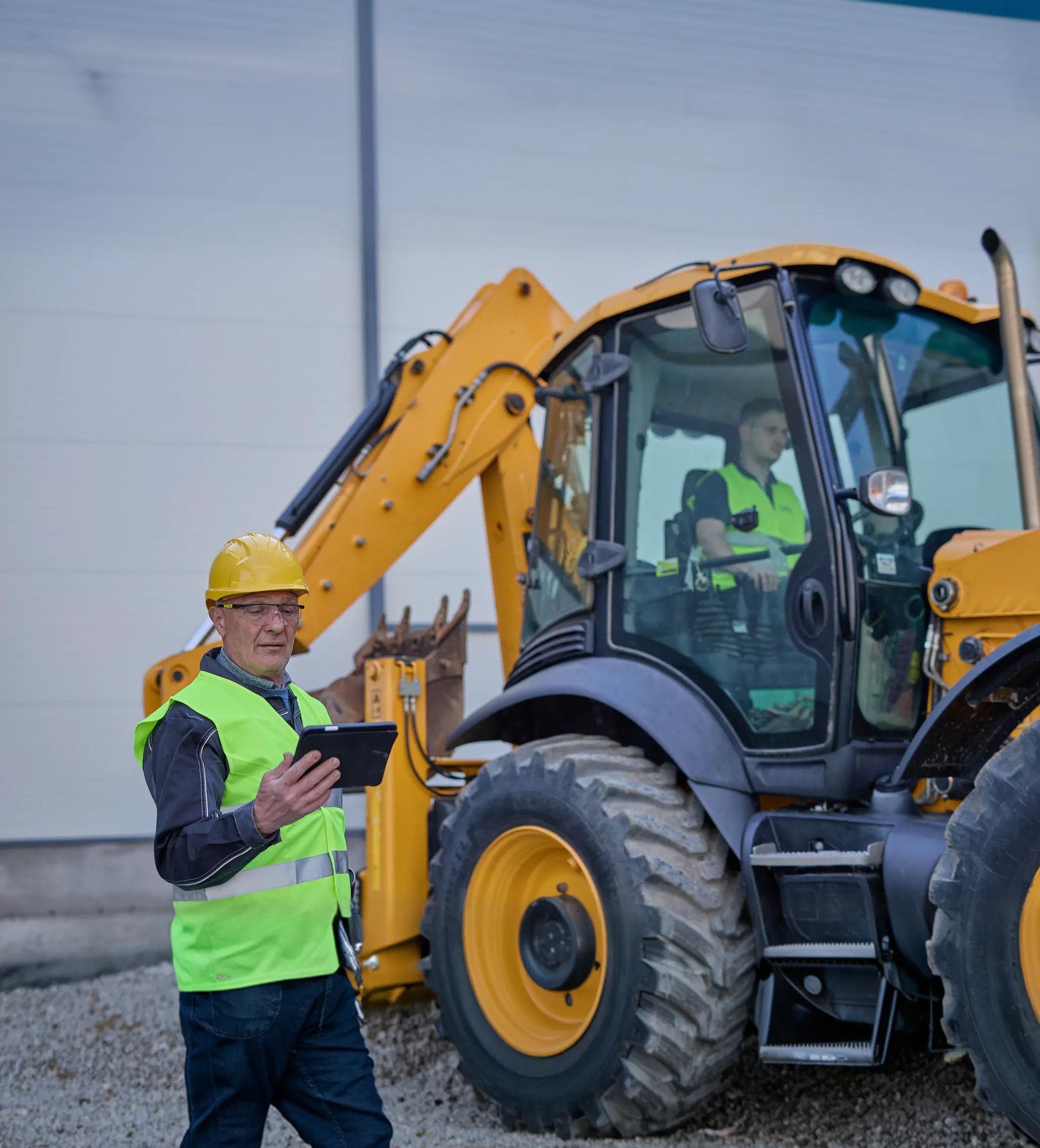Field inspector with a tablet beside a backhoe loader